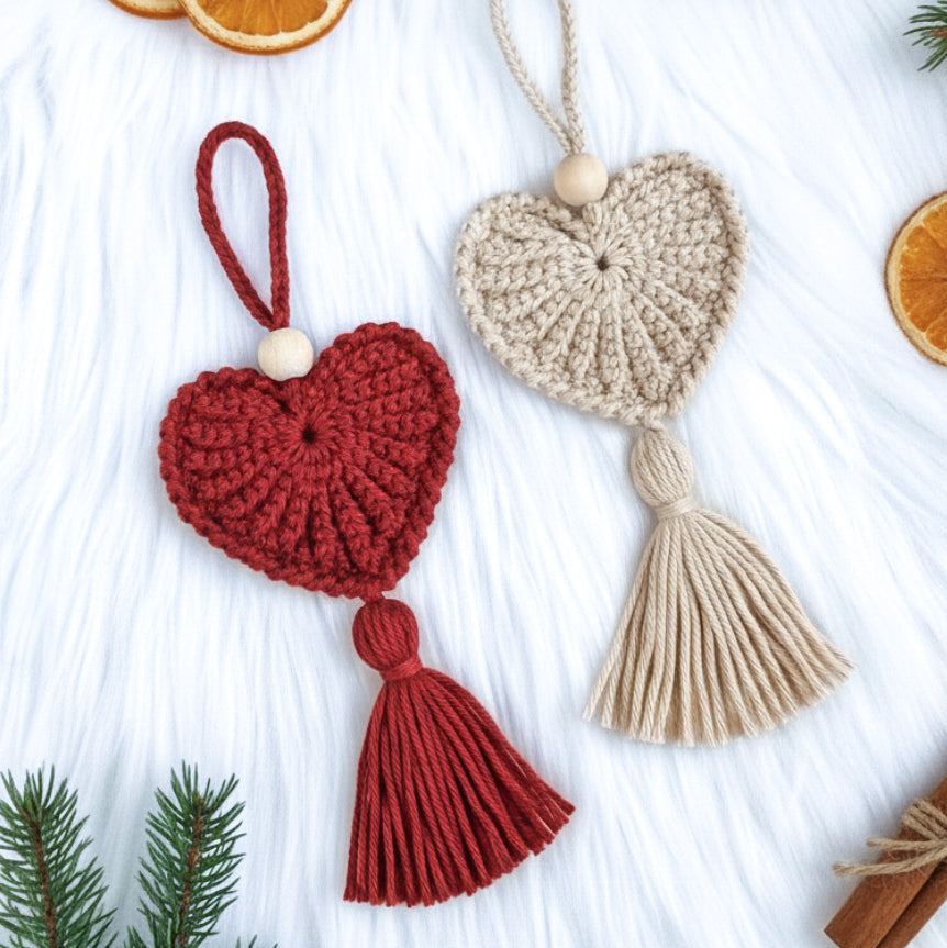 Two crocheted heart-shaped ornaments with tassels on a white surface with Christmas decorations.